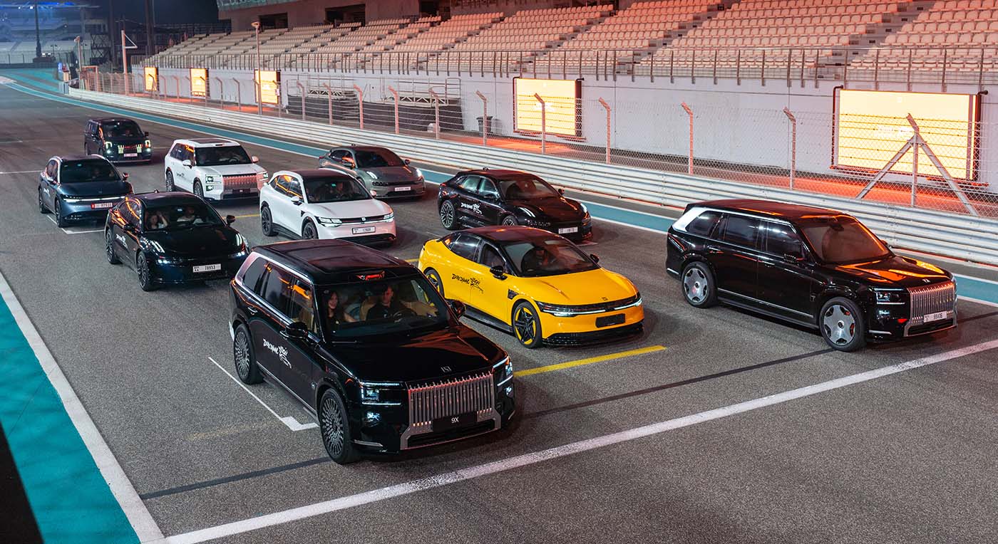 A group of luxury electric vehicles on an illuminated night race track, with a black Zeekr 009 minivan leading